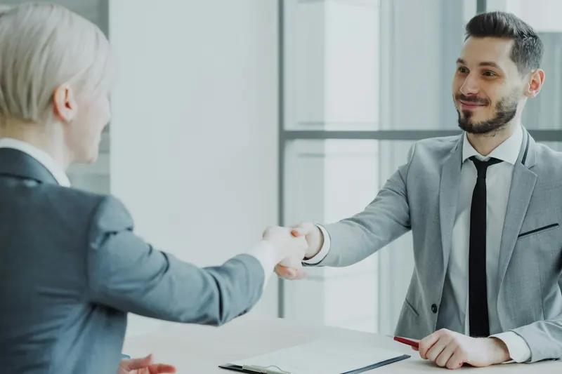Zwei Personen reichen sich im Büro über den Schreibtisch die Hand