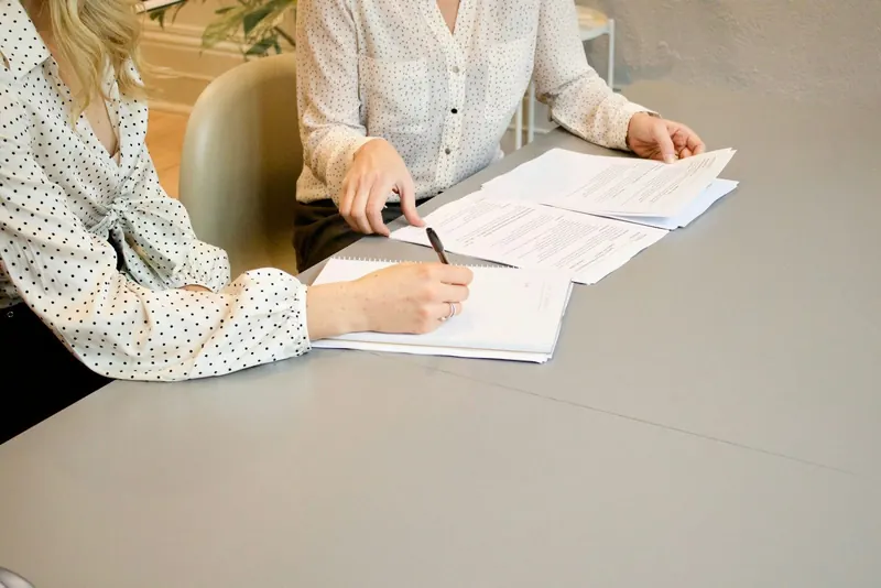 Zwei Frauen prüfen und unterzeichnen Unterlagen an einem hellen Besprechungstisch
