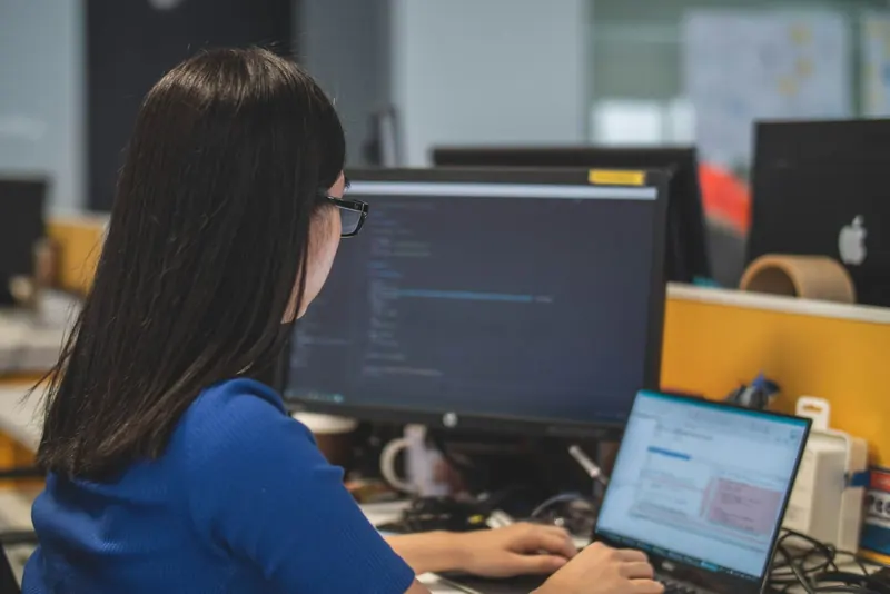 Sachbearbeiterin an einem Arbeitsplatz mit Monitor und Laptop