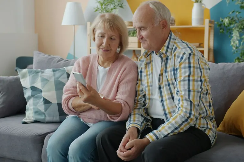 Älteres Paar sitzt auf dem Sofa und schaut gemeinsam auf ein Smartphone
