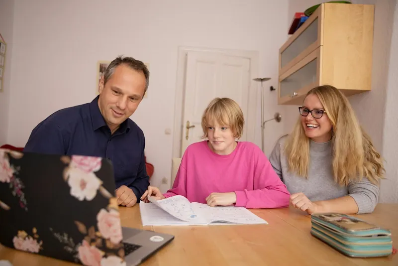Eltern und Tochter sitzen mit Unterlagen und Laptop am Esstisch