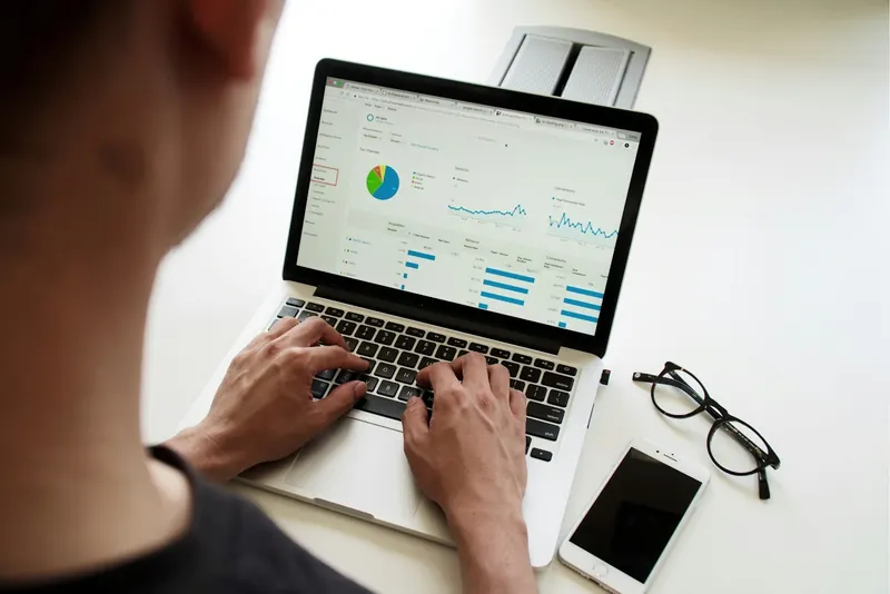 Person am Laptop mit Diagrammen und Kennzahlen auf dem Bildschirm