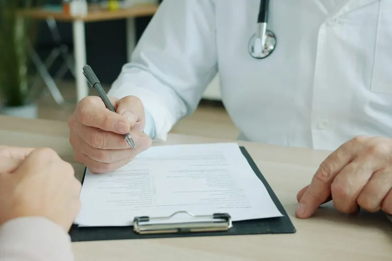 Arzt füllt im Gespräch mit einem Patienten ein Formular auf dem Klemmbrett aus